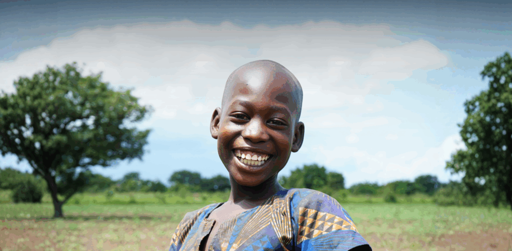 African girl smiling at camera outside with a green background.