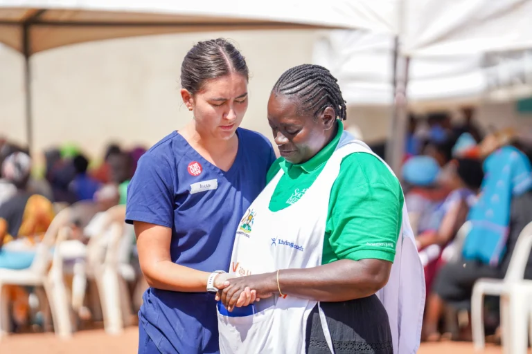 A nurse prays with a Show Mercy team member in Uganda.